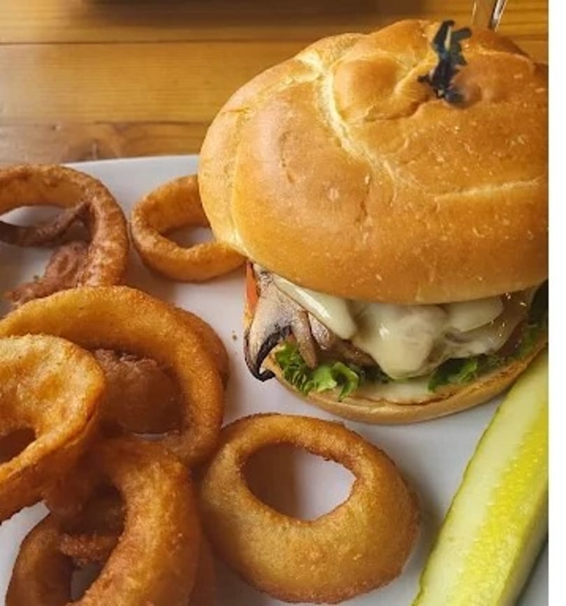 A mushroom swiss burger with lettuce and tomato, served with onion rings and a pickle spear.