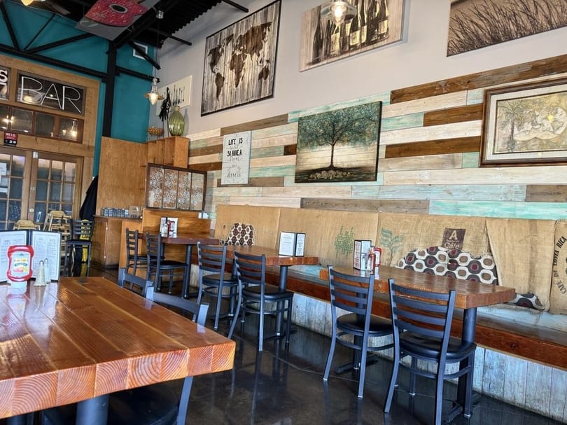Restaurant interior with wooden tables, black chairs, and a wall decorated with reclaimed wood and art.
