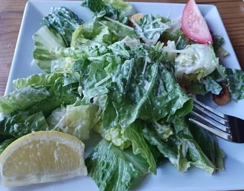 Fresh Caesar salad with romaine lettuce, dressing, a lemon wedge, and tomato slice.