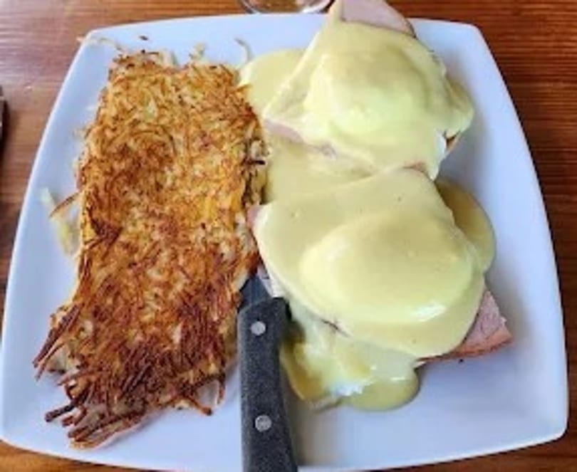 Eggs Benedict with hollandaise sauce and a side of crispy hash browns on a white plate.