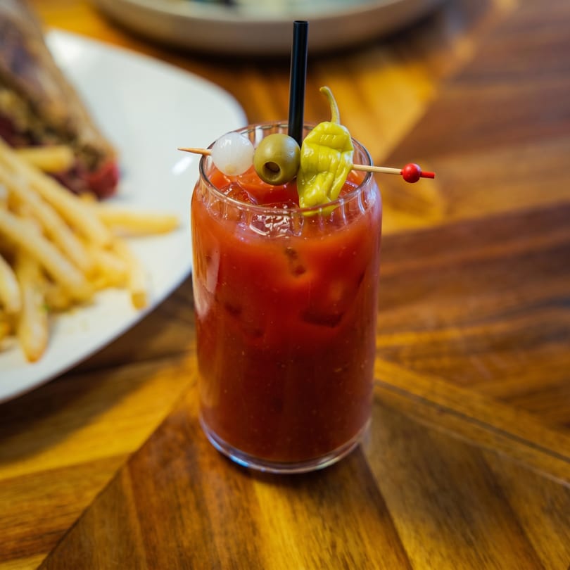 Bloody Mary cocktail garnished with an olive, pickled onion, and pepper, next to fries.