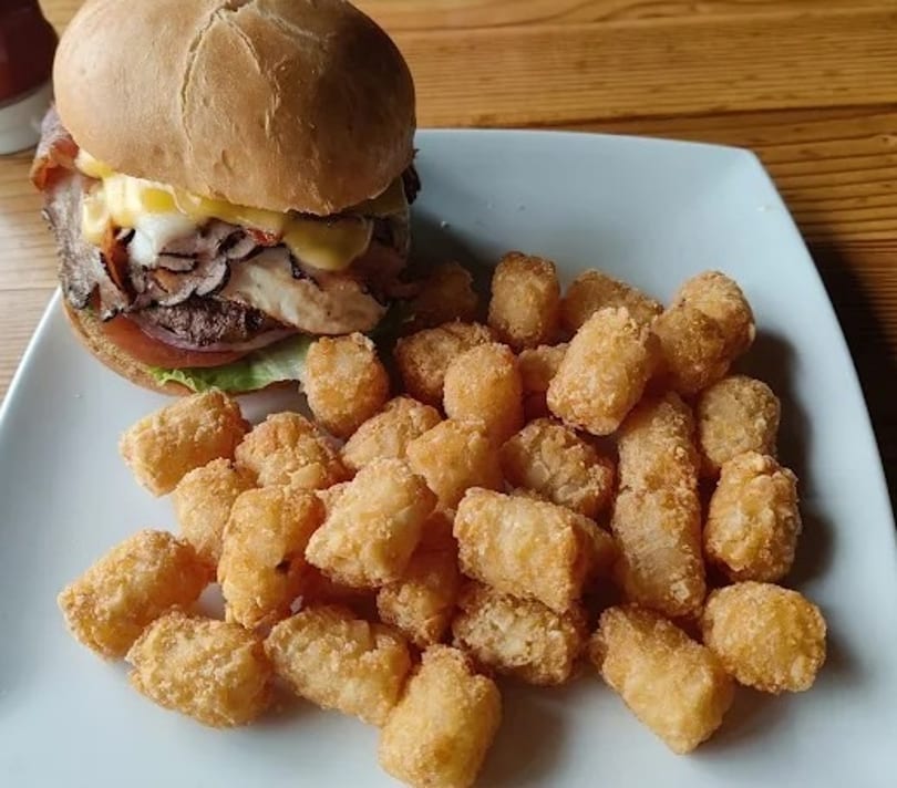 A burger with cheese, bacon, and mushrooms, served with a side of golden tater tots.