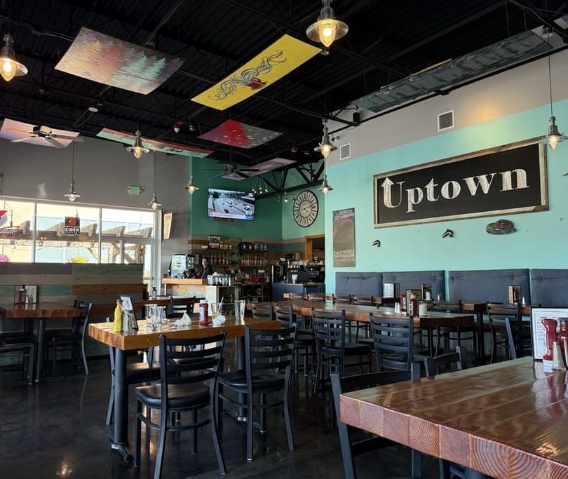 Spacious, modern restaurant interior with wooden tables, black chairs, and a large "Uptown" sign.