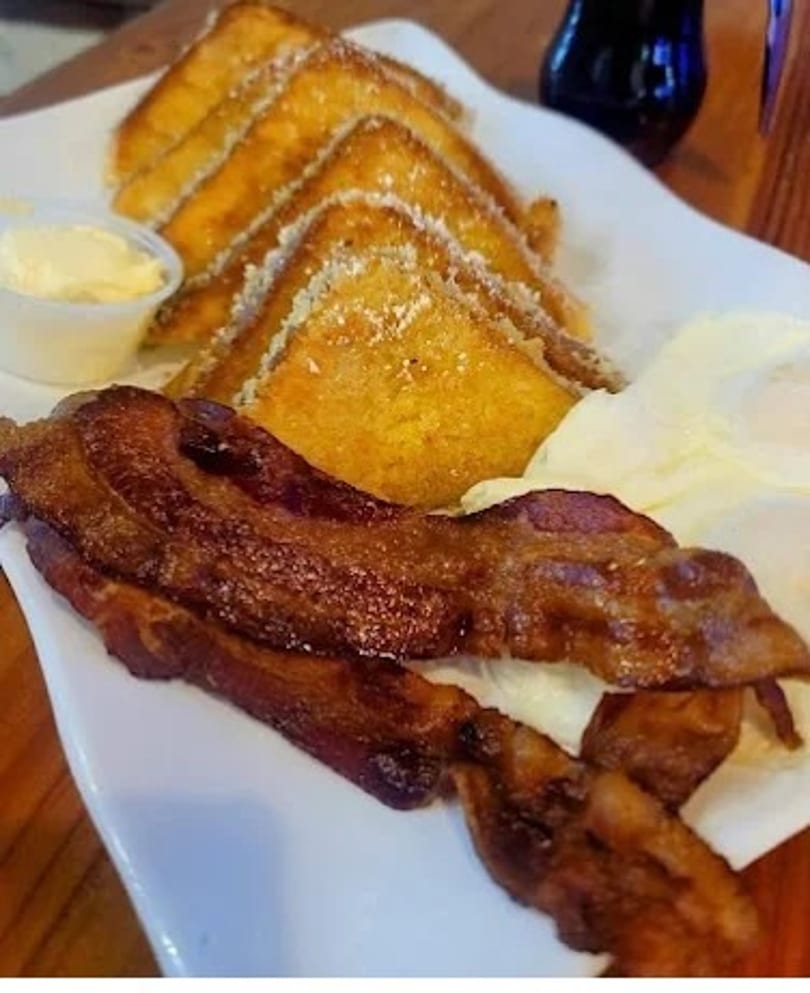 Breakfast plate with French toast, crispy bacon, scrambled eggs, and a side of butter.