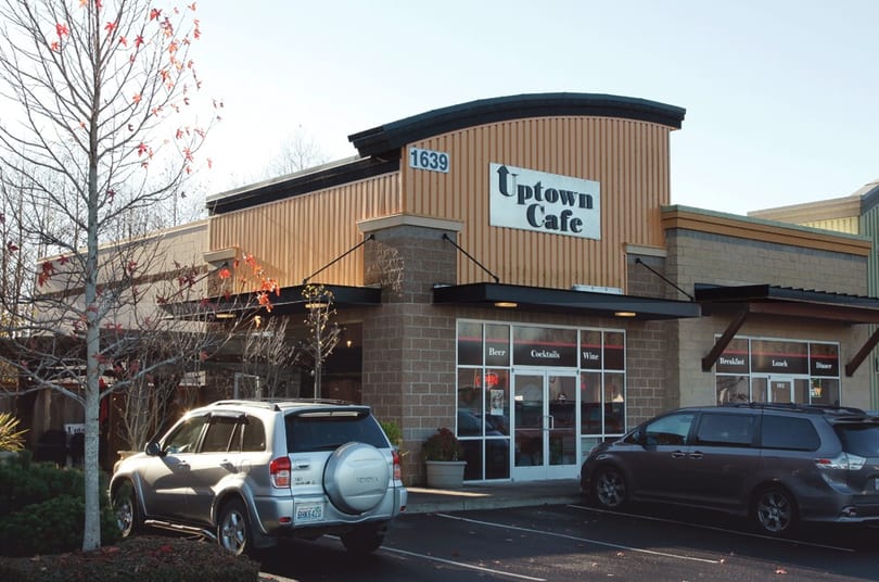 Exterior view of Uptown Cafe, a brick and wood-paneled building with parked cars in front.